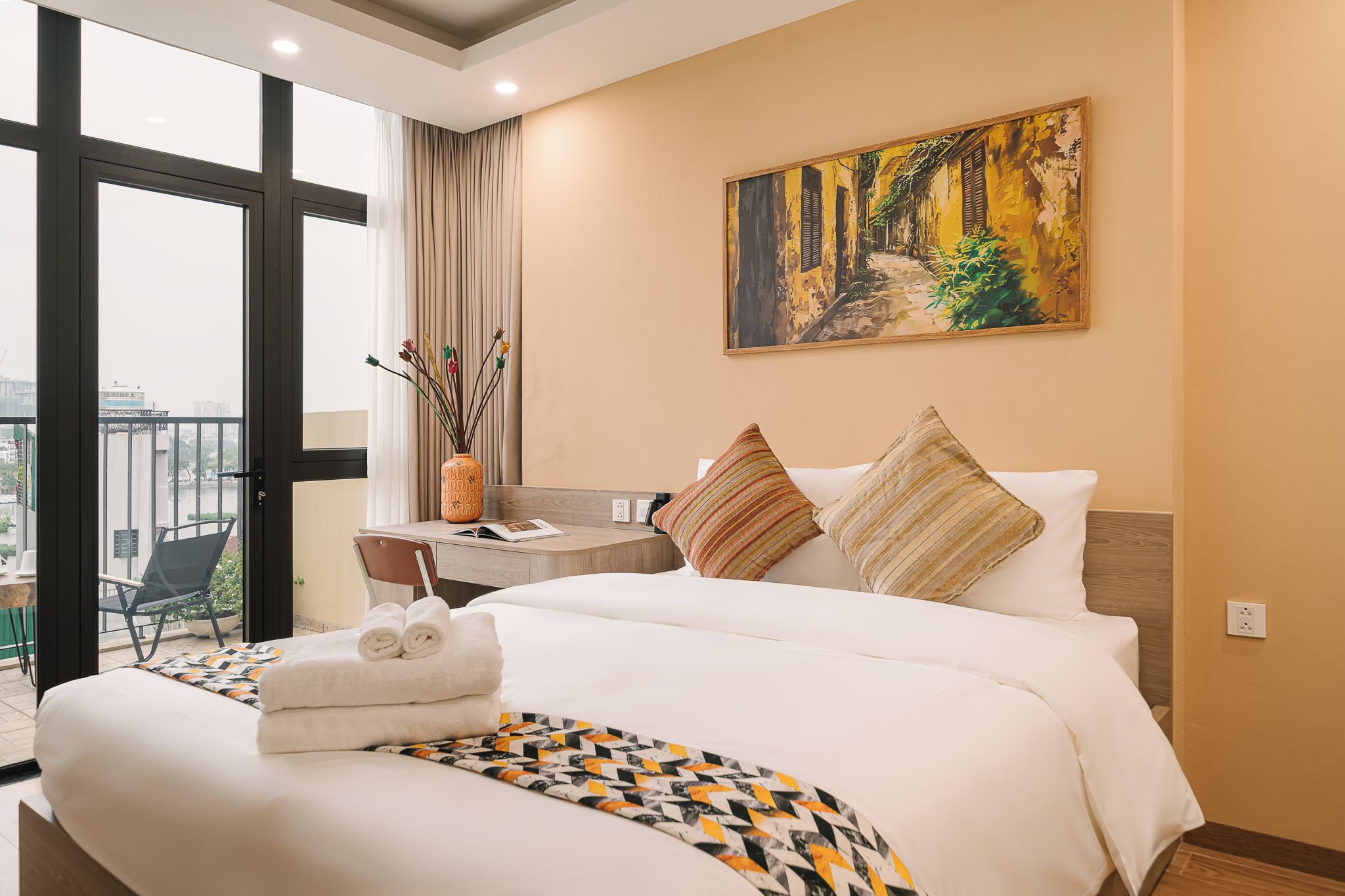 Une chambre d’hôtel avec un lit, un bureau, une chaise, un tableau et une vue sur l’extérieur.