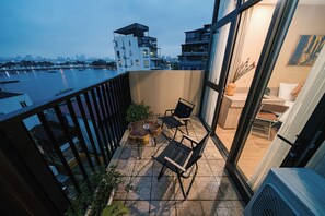 A balcony with a view of a river and city skyline, furnished with chairs and a small table. - An Yên Island (Ba Đình)