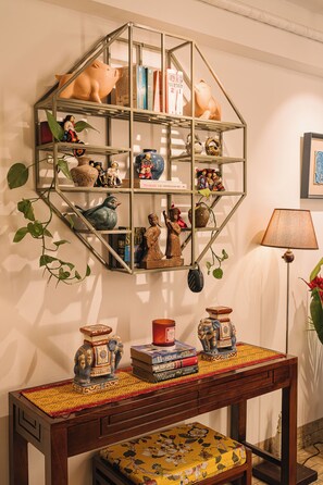 Une pièce comprenant une étagère métallique hexagonale où sont exposés des livres et des objets décoratifs, une table en bois avec un chemin de table à motifs et des livres, ainsi qu’une lampe.