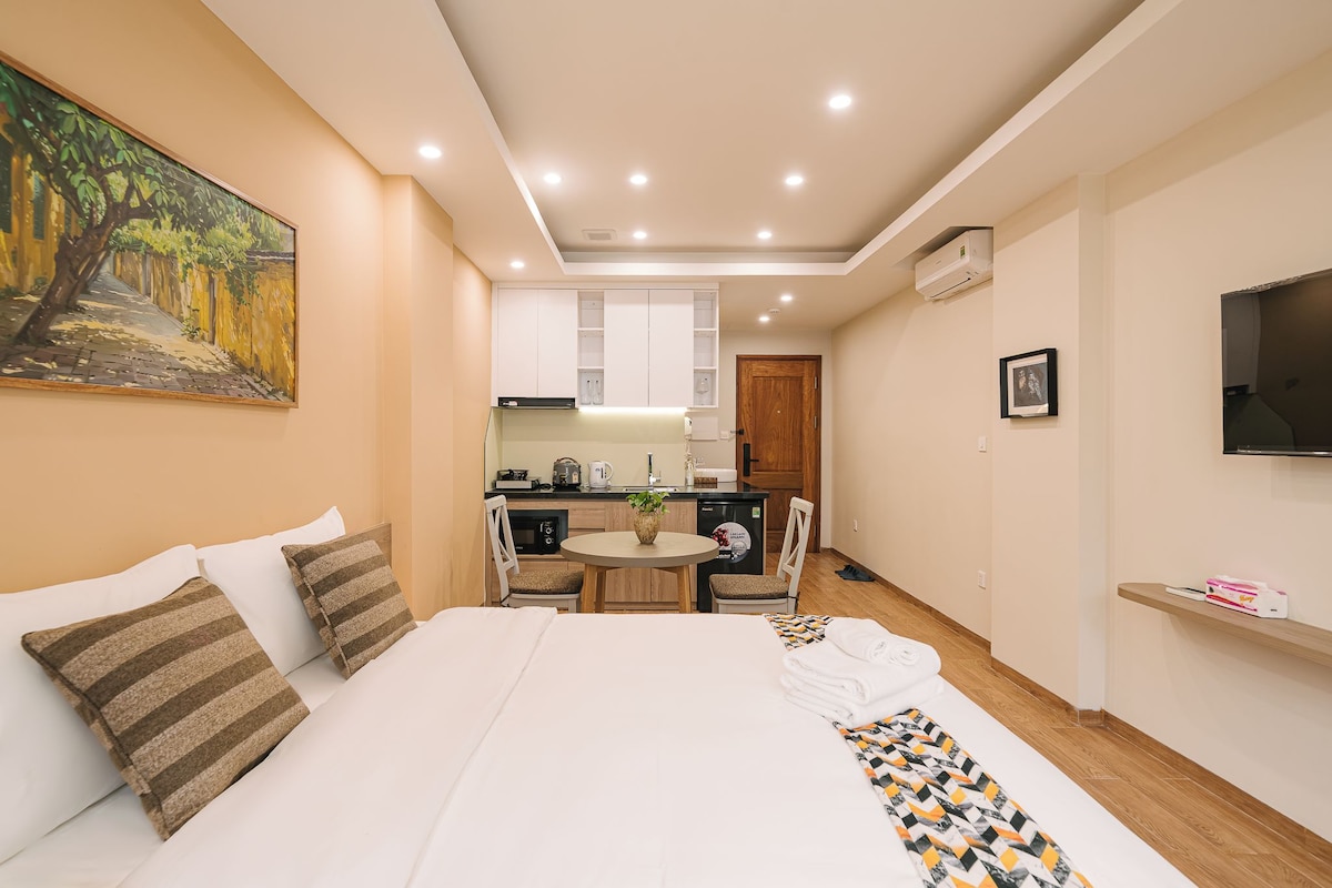 Une chambre d’hôtel comprenant un lit, une petite table à manger, un coin cuisine et un téléviseur fixé au mur.