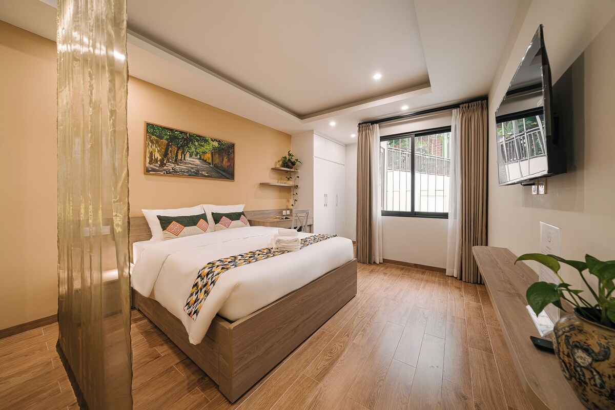 Une chambre moderne avec un grand lit, un téléviseur fixé au mur et une fenêtre avec des rideaux.