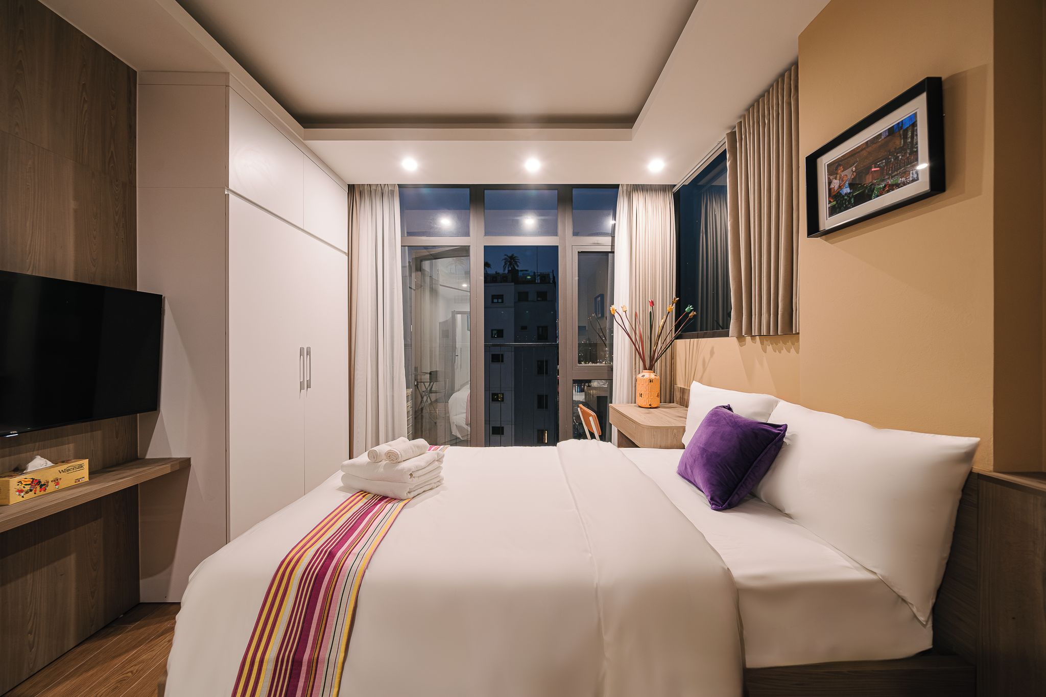 A hotel room with a bed, a TV, a desk, and a window with curtains.