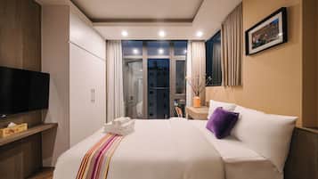 A hotel room with a bed, a TV, a desk, and a window with curtains.