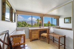 Ein Zimmer mit Schreibtisch, zwei Stühlen, einem Fenster mit Blick auf Grünflächen und Berge sowie gerahmten Bildern an der Wand.