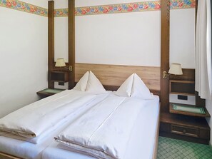 Ein Hotelzimmer mit einem hölzernen Kopfende, zwei Nachttischen mit Lampen, einem Bett mit weißen Leinen und einer floralen Bordüre an der Wand.