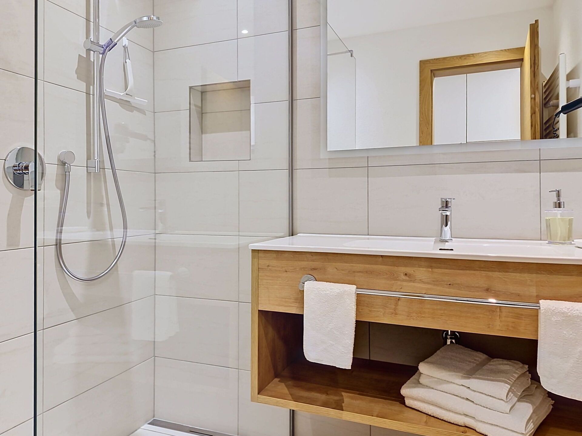 Une salle de bain moderne avec une douche à parois de verre, un meuble-lavabo en bois avec un miroir et un porte-serviettes.