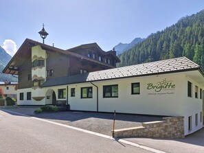 Ein zweistöckiges Gebäude mit einem Schild, auf dem 'Brigitte Ferienhaus' steht, vor einer Bergkulisse.