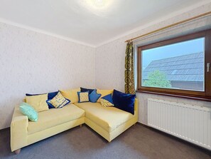 Ein Eckzimmer mit einem gelben Sofa, gemusterten Kissen, einer Heizung und einem Fenster mit Blick auf ein Gebäude.