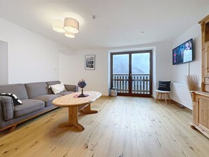 A living room with a sofa, a round wooden table, a television, and a view through a glass door.