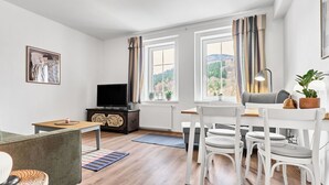 Un salon moderne avec un téléviseur, un coin repas avec des chaises et un canapé.