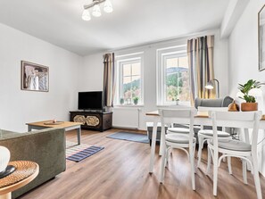 Ein modernes Wohnzimmer mit Fernseher, Essbereich mit Stühlen und einer Couch.