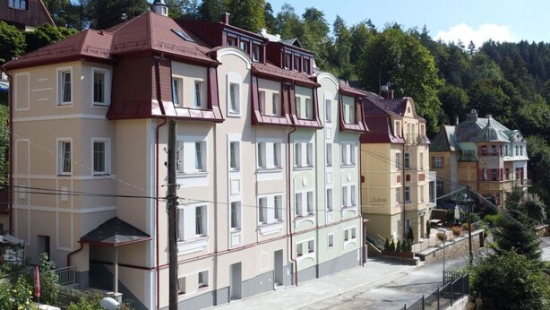 Une rangée d’immeubles à plusieurs étages dotés de balcons, un ciel dégagé et des arbres en arrière-plan.