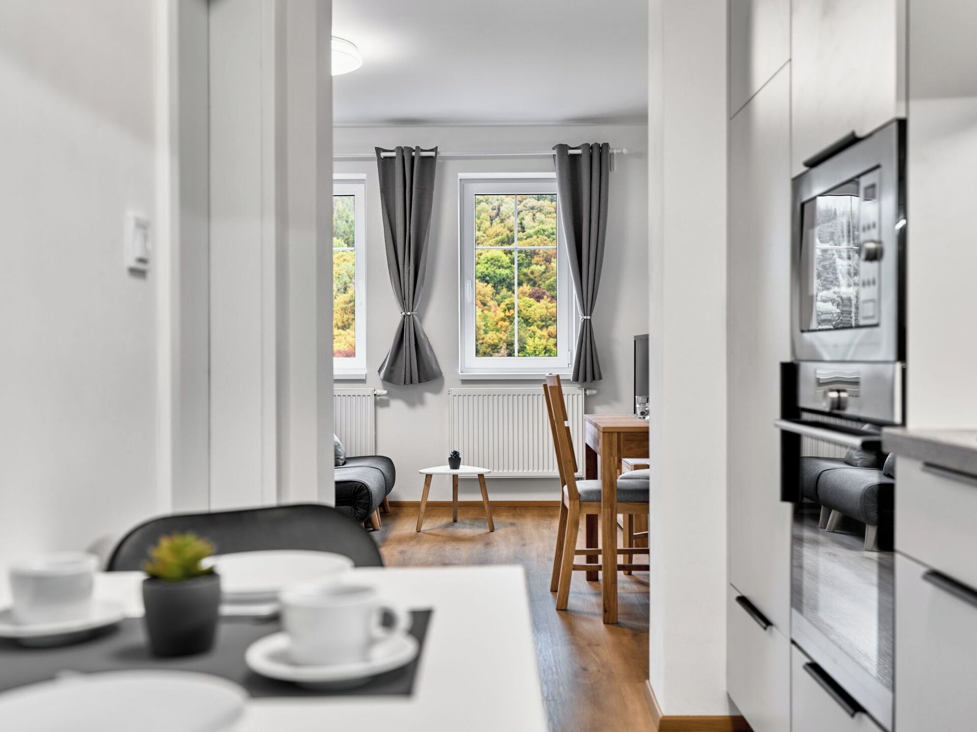 Una cocina moderna con comedor, vistas a árboles a través de las ventanas y una pequeña mesa con una planta.