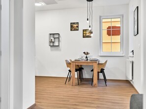 Uma área de refeições com mesa e cadeiras de madeira, uma janela com vista e um candeeiro fixado na parede.