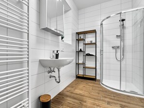 Un baño moderno con un lavamanos blanco, suelo de madera y cabina de ducha de vidrio.