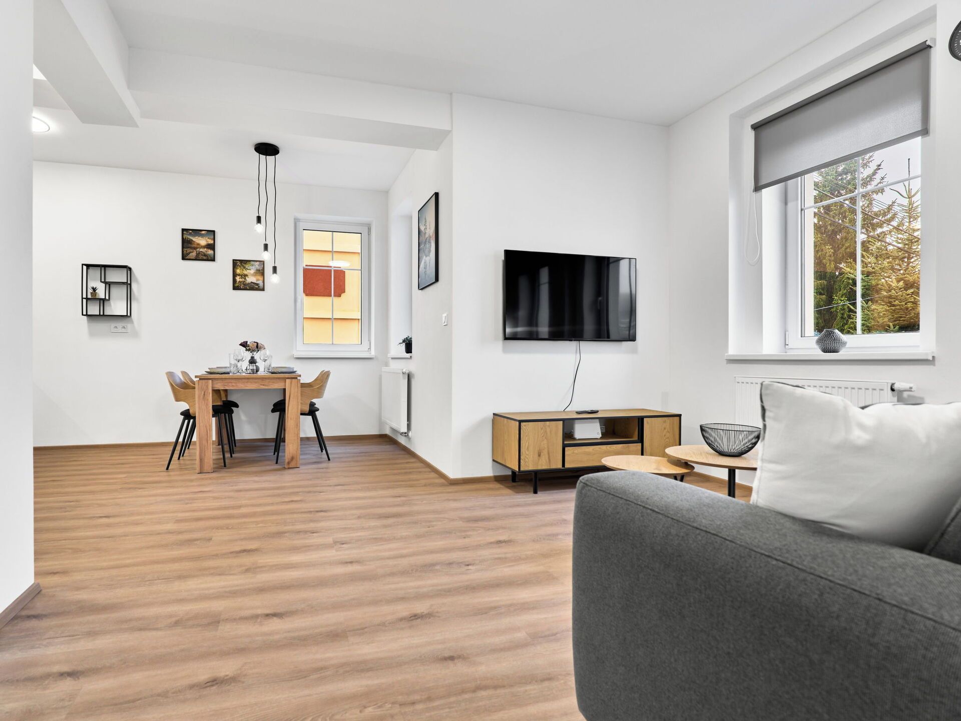 Una sala moderna con un sofá gris, una mesa de comedor de madera y un televisor montado en la pared.