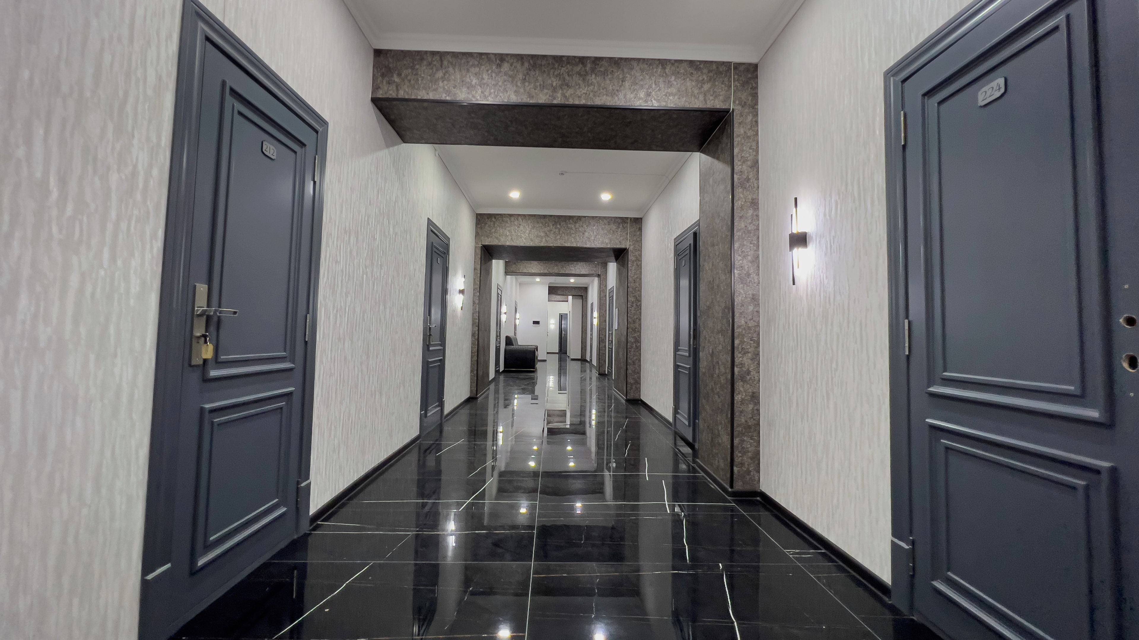 Pasillo de hotel con puertas oscuras, paredes claras y un suelo brillante.