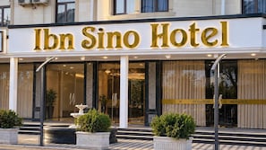 L’extérieur de l’hôtel Ibn Sino se distingue par son entrée imposante, ses grandes portes vitrées et une fontaine située au premier plan.