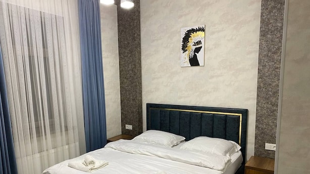 Ein Doppelbett mit weißen Leinen und zwei Handtüchern, ein Kopfteil mit goldener Zierleiste, ein kleiner Nachttisch aus Holz und ein Wandbild.