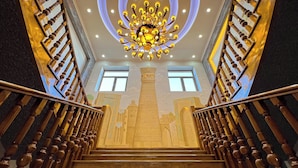 Una imponente escalera con candelabro, barandillas de madera y un detallado mural.