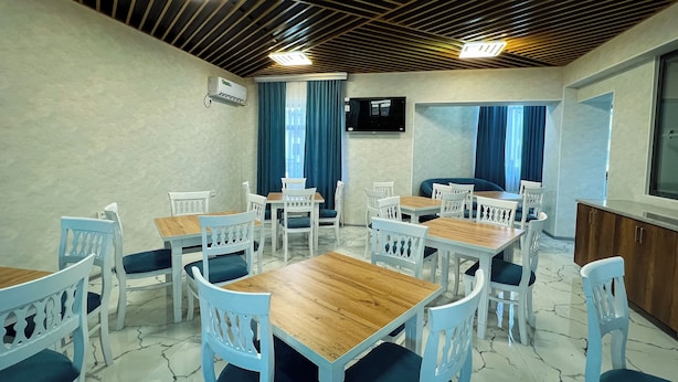 Un comedor con mesas de madera y sillas blancas, unidades de aire acondicionado en las paredes y un televisor montado.