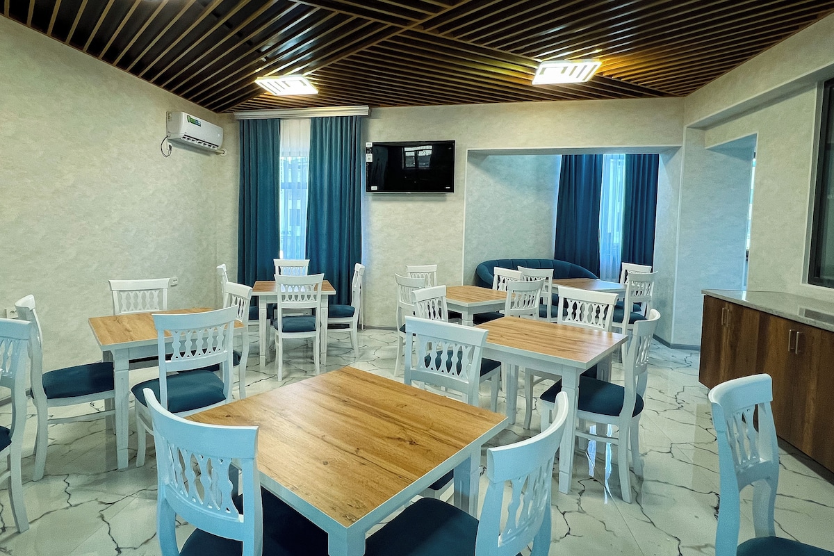Un espace repas avec des tables en bois et des chaises blanches, des climatiseurs fixés aux murs et un téléviseur accroché au mur.