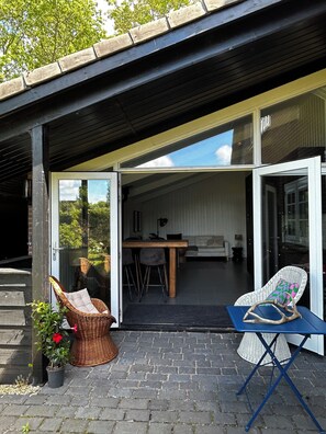 En åben patio med et spisebord, stole, en fletstol, en potteplante og et blåt foldbart bord med en pynteting.