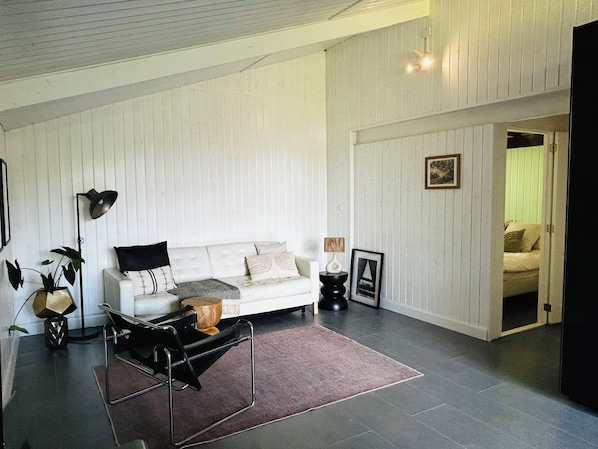 A living room with a white sofa, a coffee table, and a lamp. There is a door leading to another room.