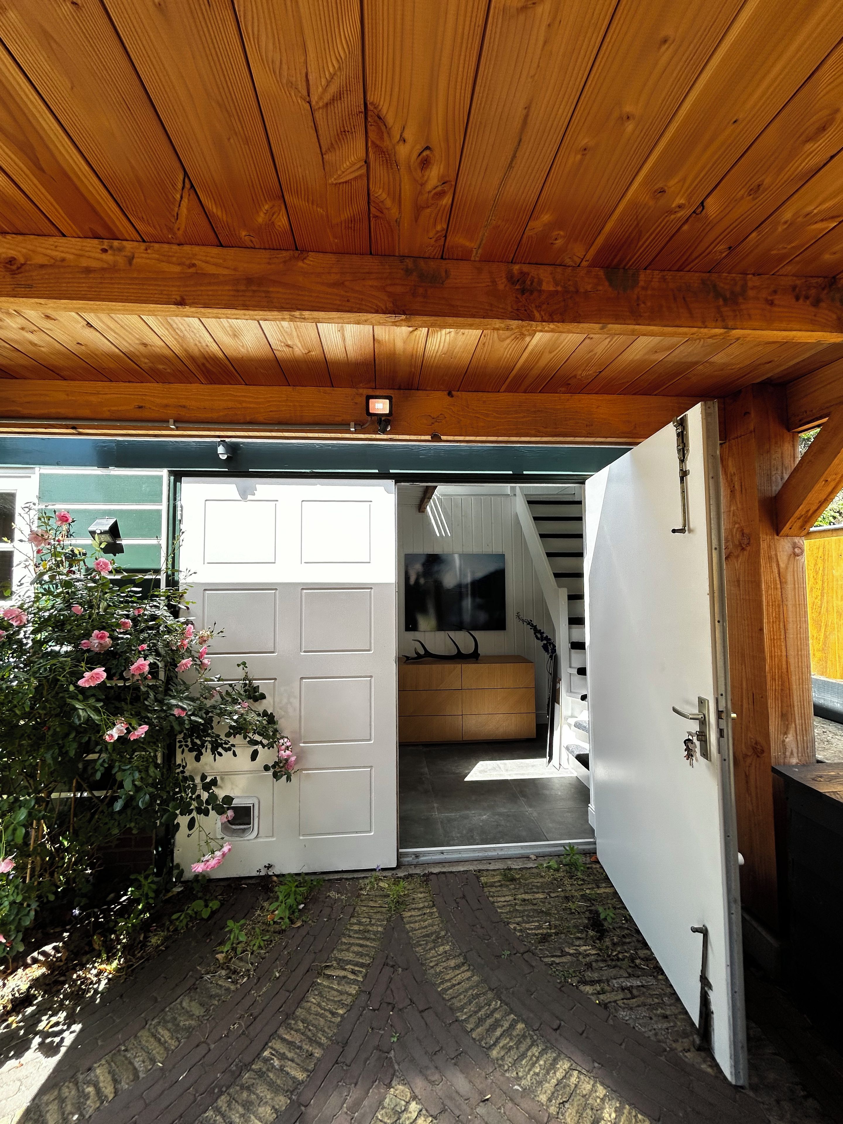 Un plafond en bois, une porte blanche, un meuble en bois et un chemin pavé de briques.