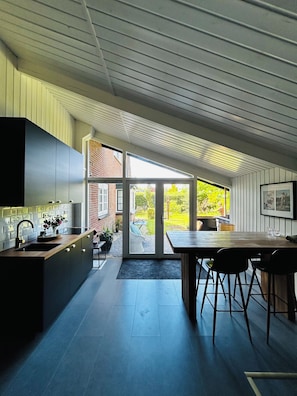 A modern kitchen with a large island, a dining area with a table and chairs, and a sliding glass door leading to a garden.