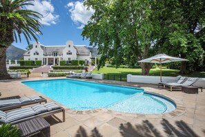 A swimming pool with lounge chairs and a large house in the background. - Exclusive & Secure, 5-Star Private Country House Estate in Constantia, Cape Town (Cape Town)