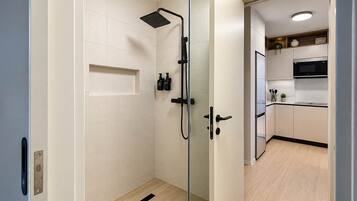 A modern bathroom with a glass shower enclosure, a white tiled wall, and a wooden floor.