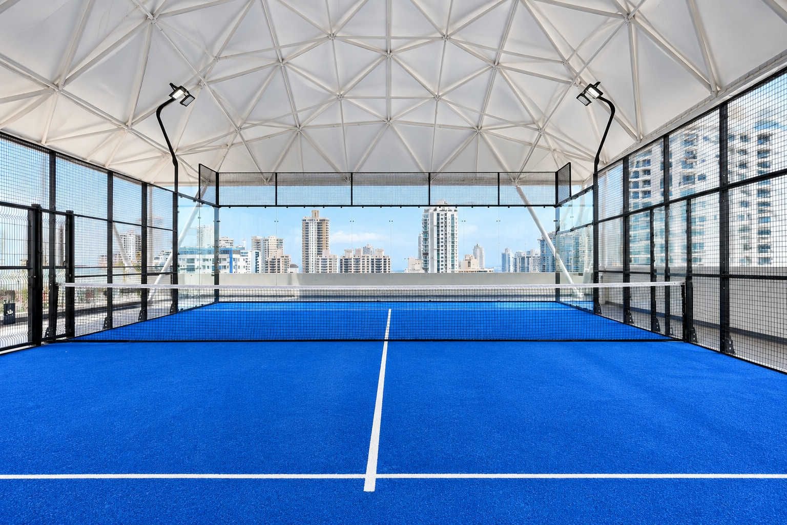 An indoor tennis court with a clear view of a city skyline through the netting.