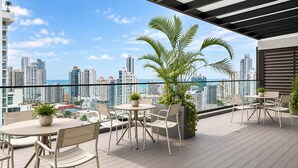 Terraza en la azotea con mobiliario exterior, plantas en macetas y vista panorámica de la ciudad.