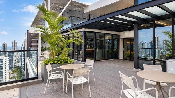 Una terraza en la azotea con mobiliario exterior, una cocina de cristal y vistas al horizonte de la ciudad.