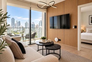 Een moderne woonkamer met een grote televisie, een bank, een salontafel en uitzicht op de stad.