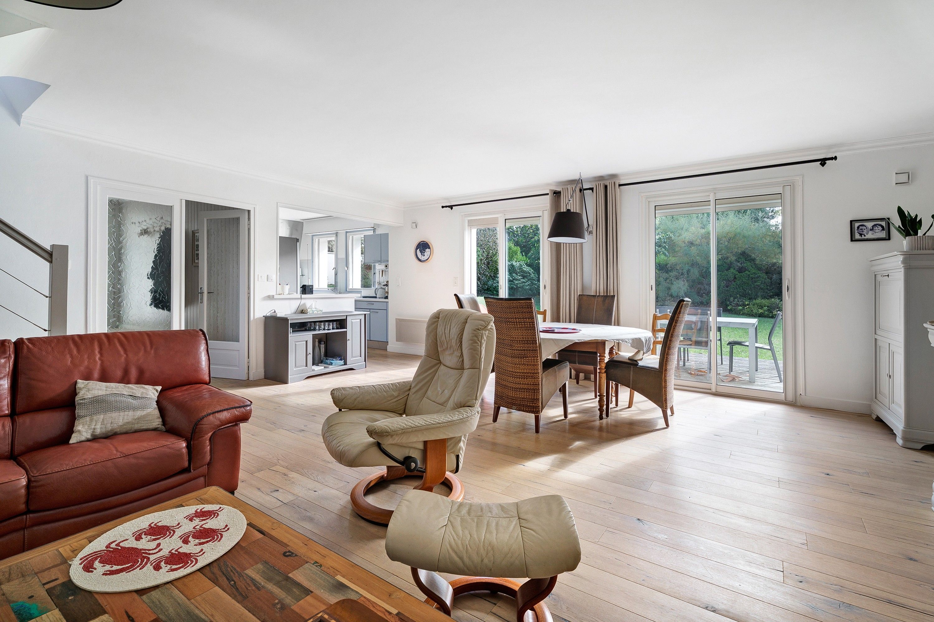 A spacious living area with a leather sofa, a dining table with chairs, and a kitchen in the background.