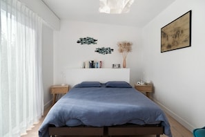 Ein Schlafzimmer mit einem Bett, Nachttischen, einer Wanduhr und einem gerahmten Kunstwerk.