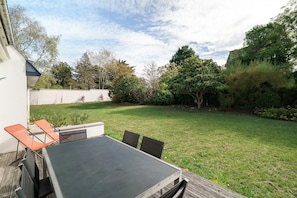 Eine Terrasse mit Tisch und Stühlen, umgeben von einem Rasen und Bäumen.