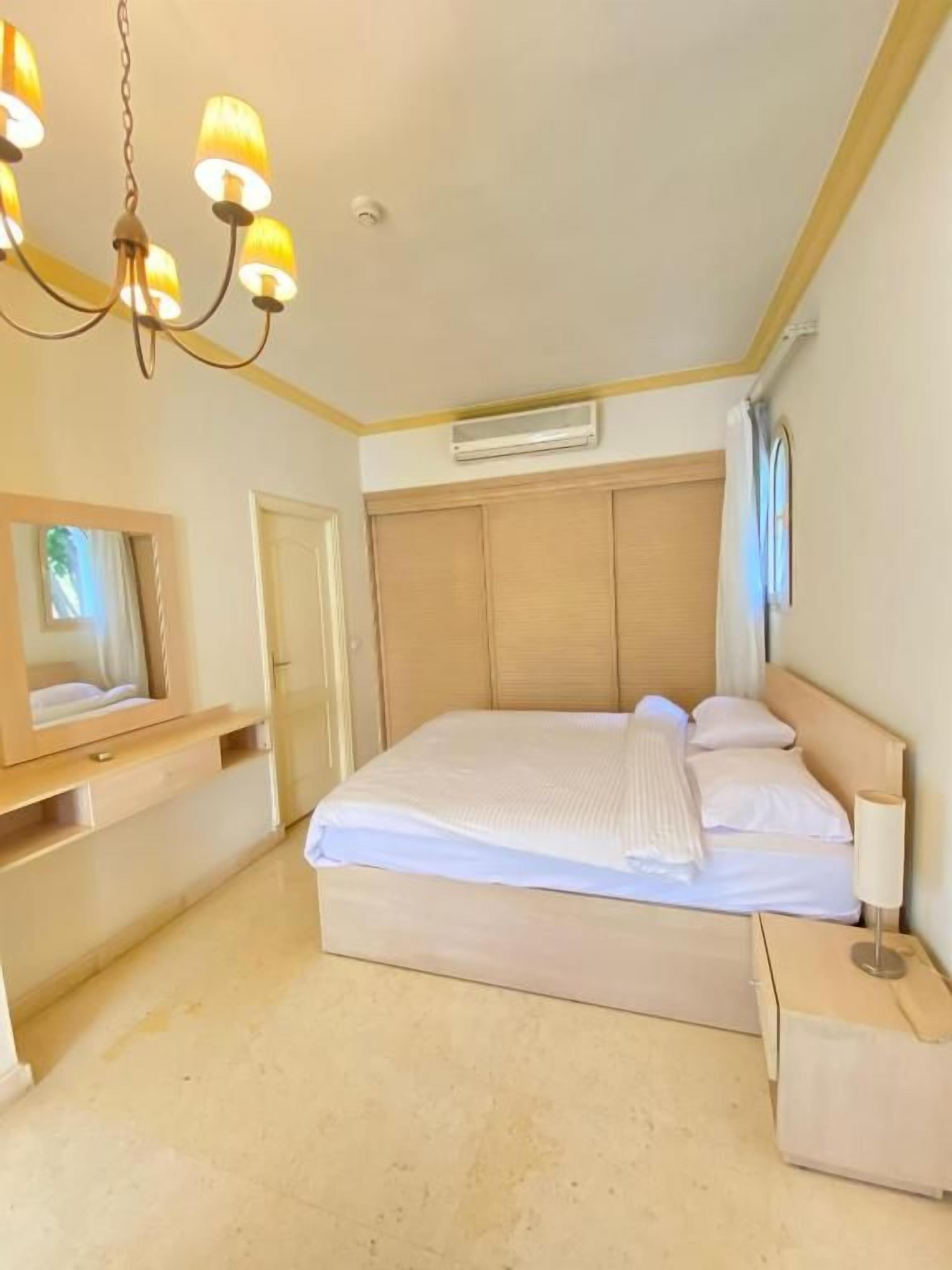 A bedroom with a large bed, bedside tables, a mirror, and a chandelier.