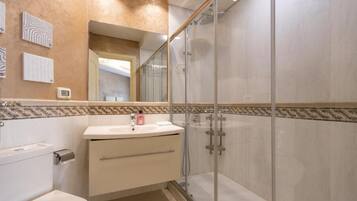 A modern bathroom with a glass-enclosed shower, a toilet, and a vanity with a mirror.