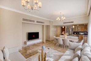 A modern living room with a flat-screen TV, a dining area with a table and chairs, and a kitchen in the background. - Elsafwa resort (new.cairo)