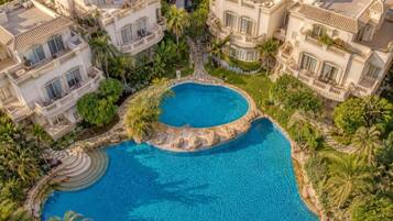 A large, circular swimming pool surrounded by lush greenery and multiple multi-story buildings with balconies.