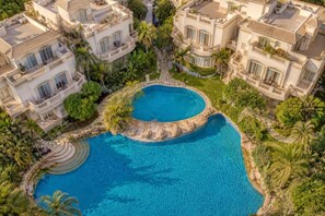 A large, circular swimming pool surrounded by lush greenery and multiple multi-story buildings with balconies. - Elsafwa resort (new.cairo)