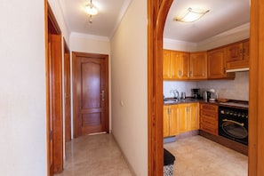A hallway leading to a kitchen with wooden cabinets, a stove, and a trash bin. - South-Facing Duplex in Los Cristianos (Los Cristianos)