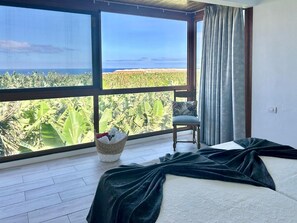 A bedroom with a large window, a bed, a chair, and a basket of items. - Holiday Home in La Palma for 4 (Fuencaliente de la Palma)