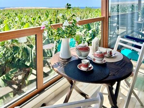 A balcony with a table set for tea, a vase with flowers, and a view of a green field. - Holiday Home in La Palma for 4 (Fuencaliente de la Palma)