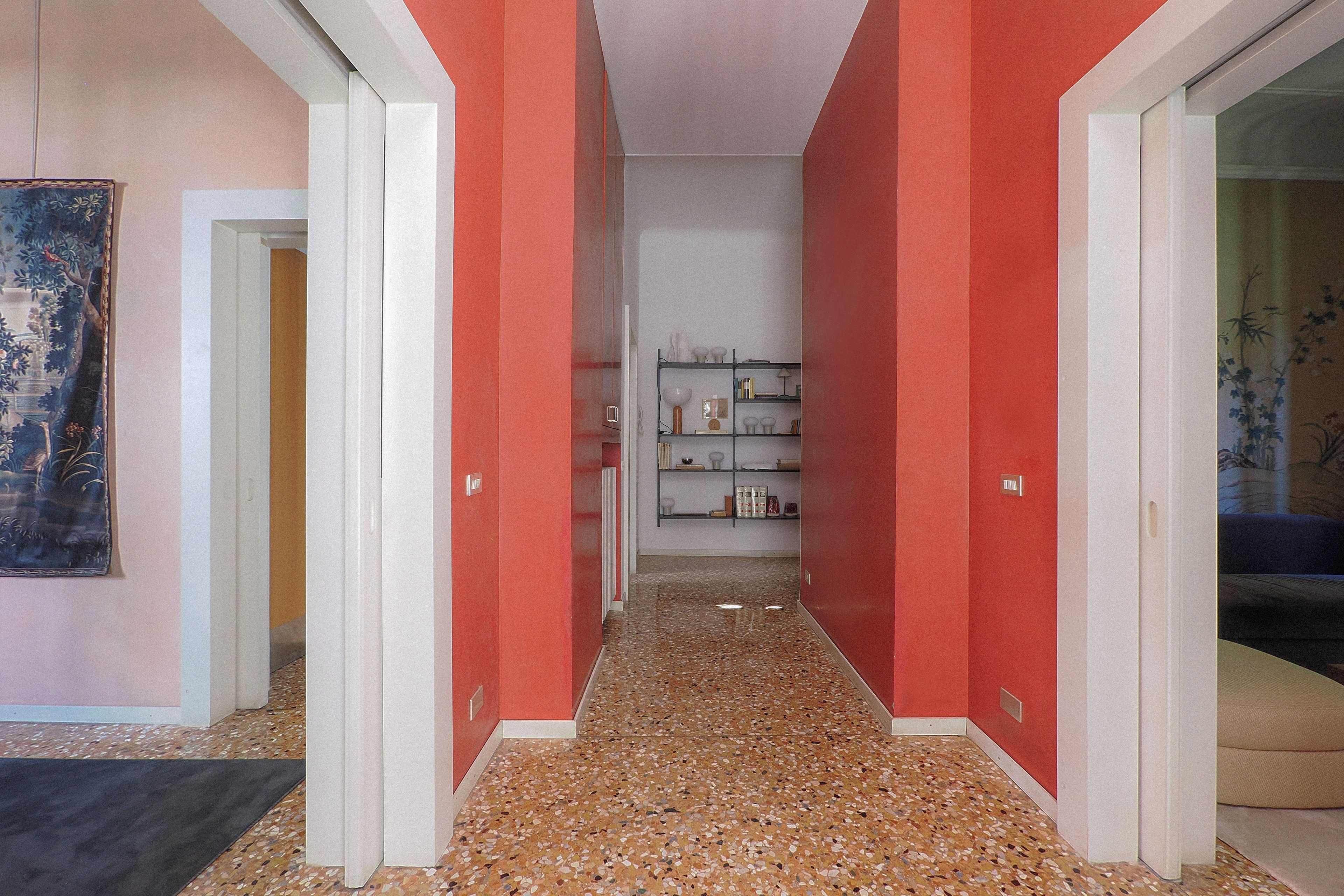 Un corridoio con pareti rosse, pavimento piastrellato e una libreria in lontananza.