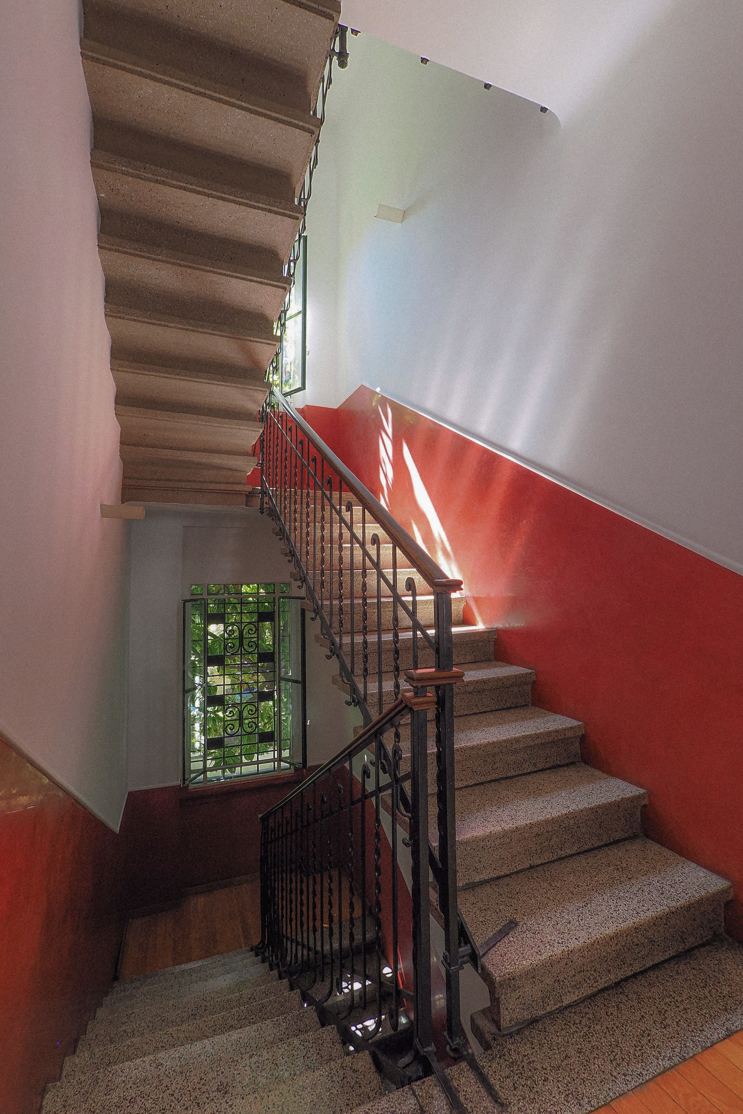 Una scala con ringhiera rossa e inferriata, che conduce a un pianerottolo con una finestra verde.