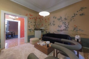 A living room with a sofa, ottoman, and coffee table. There is a wall with a floral mural and a ceiling light. - Contempora - Casa Osti - Designer Villa with Garden in the City Center (Milano)